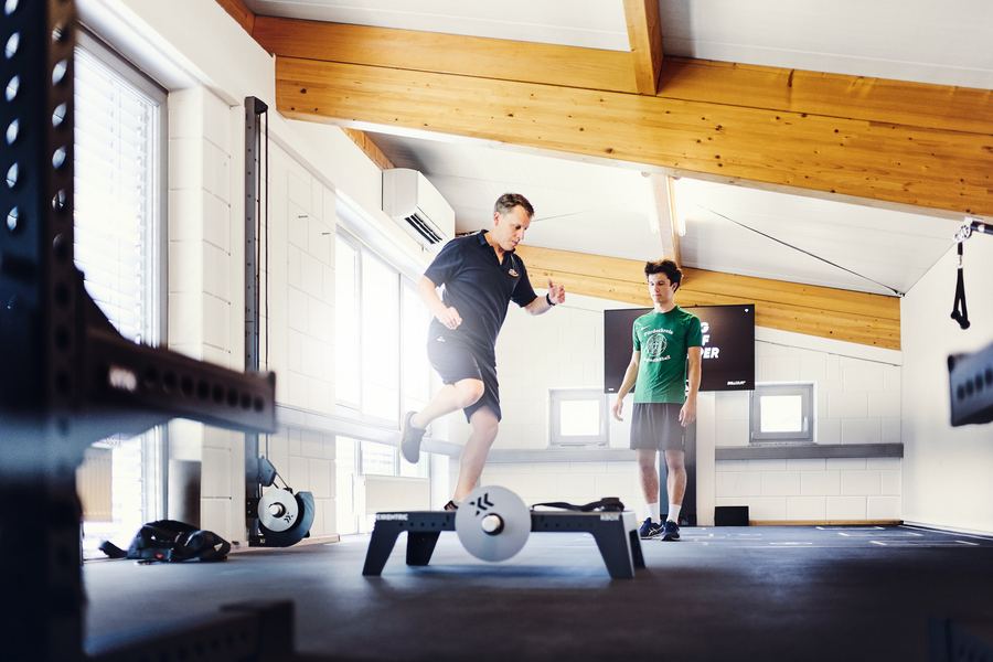 Therapeut begleitet Sportler beim Ausfallschritt-Training mit der Hantelstange