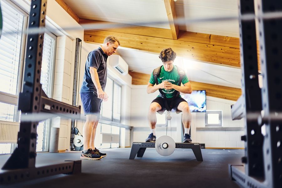Therapeut beobachtet Sportler bei der Kniebeuge im Kraftrack