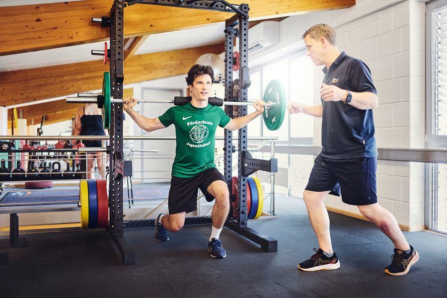 Therapeut sichert Sportler beim Ausfallschritt mit der Langhantel